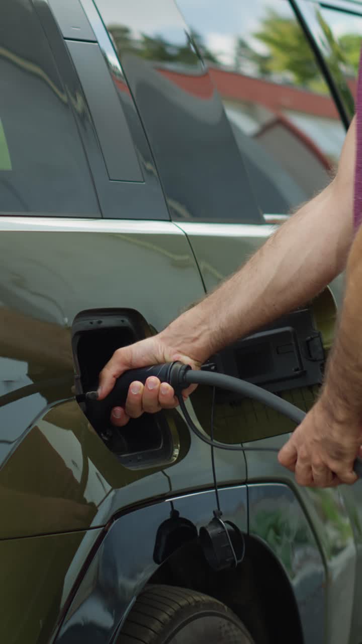 Vertical video Close up of driver attaching electric cable to recharge electric SUV car