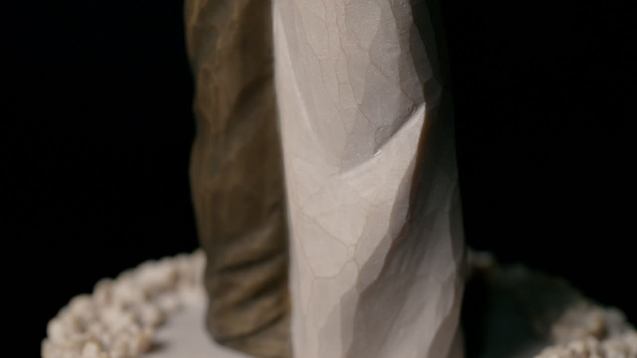 Elegant close-up shot of a wooden wedding cake topper depicting an embracing couple, set against a dark background with soft lighting highlighting the tender detail