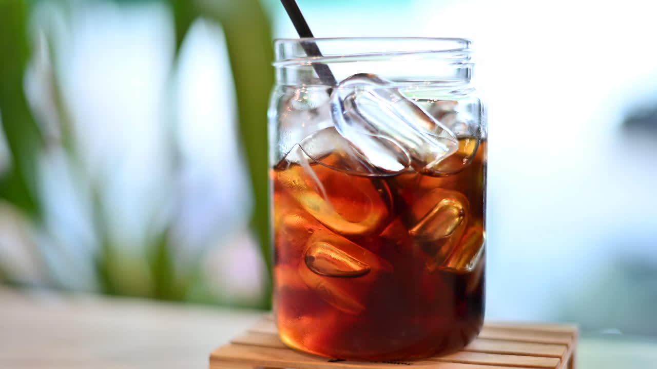 Primo piano di un caffè freddo con ghiaccio su una palette di legno con sfondo tropicale