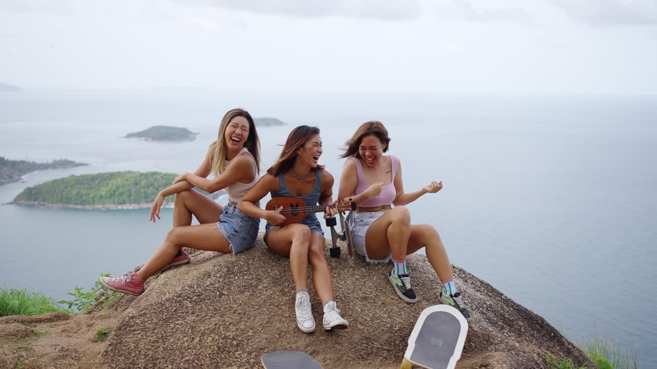 un grupo de 4k de mujeres asiáticas sentadas en el pico de la montaña tocando el ukulele y bailando juntas.