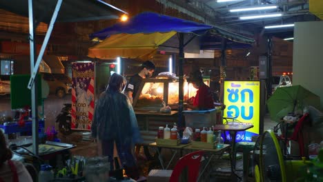 food vendor with customers on busy street in thailand during rainy stormy night