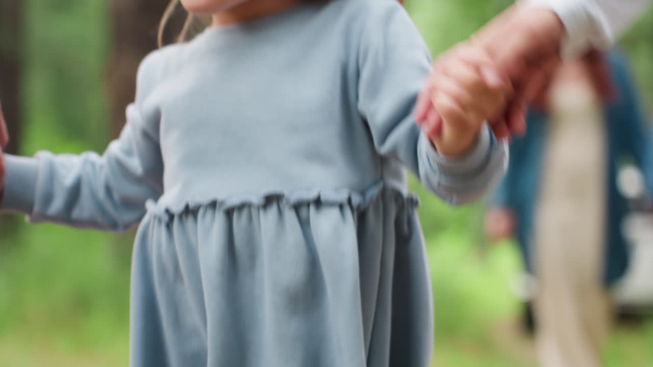 사랑과 설렘, 자유, 어린 시절의 에너지를 표현하며 산들바람에 부드러운 파란색 드레스를 입고 형제자매에게 안긴 행복한 어린 소녀가 부모님 뒤에서 푸른 숲길을 즐겁게 걷고 있어요.