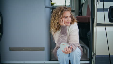 camping woman holding mug with beverage sitting camper van stairs at vacation