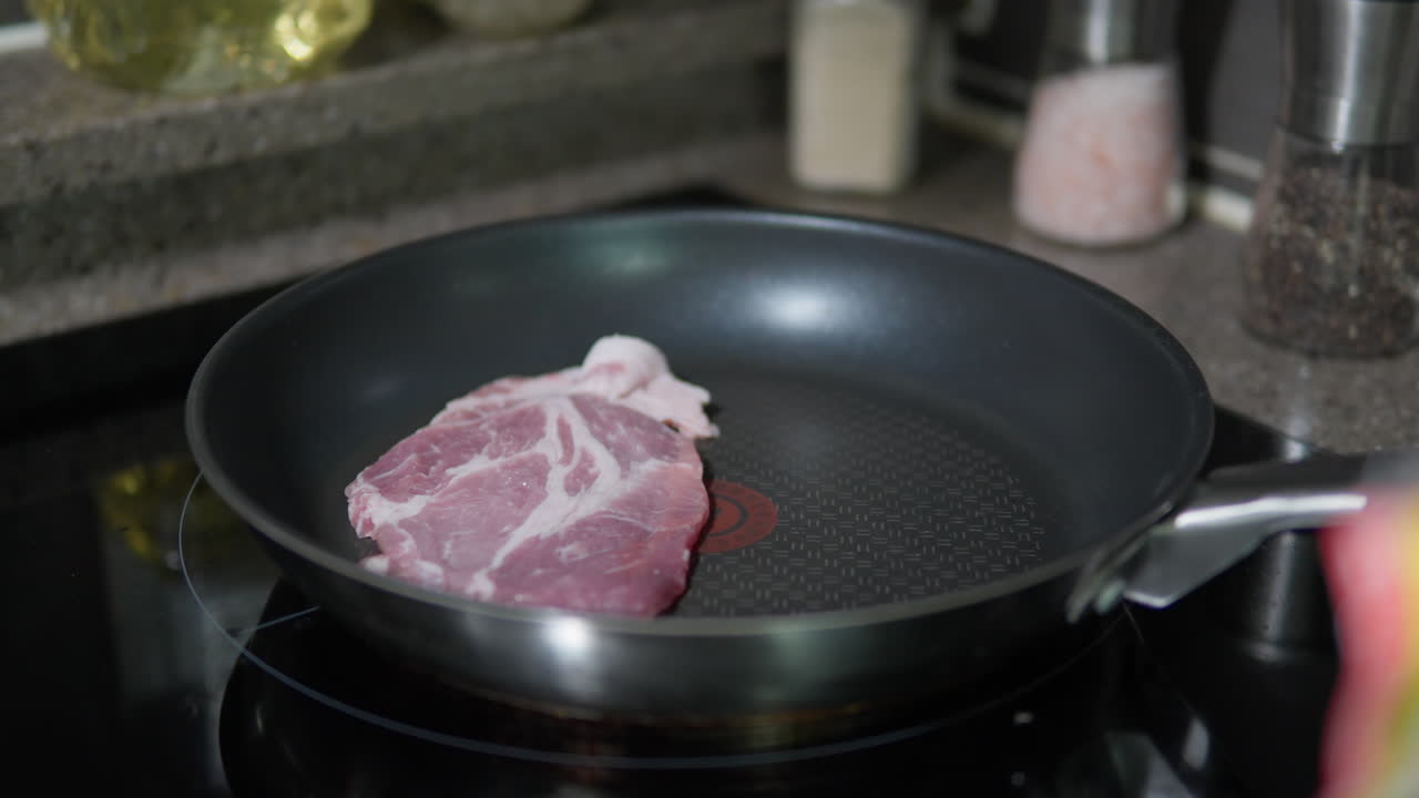 Man's Hand Using Tongs to Put Thin Raw Pork Slice on Frypan