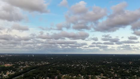 an aerial time lapse over a residential neighborhood. the drone trucks left and pans right as the clouds move towards the left. the drone is high enough to see cars and the horizon. it is a sunny day