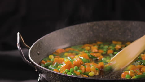 Mezcla-De-Verduras-Frescas-En-Una-Sartén-Con-Una-Colorida-Combinación-De-Guisantes-Y-Zanahorias-Con-Fondo-Negro-Y-Filmada-En-4k