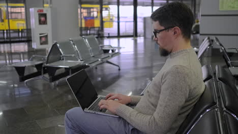 man working on laptop in airport waiting area