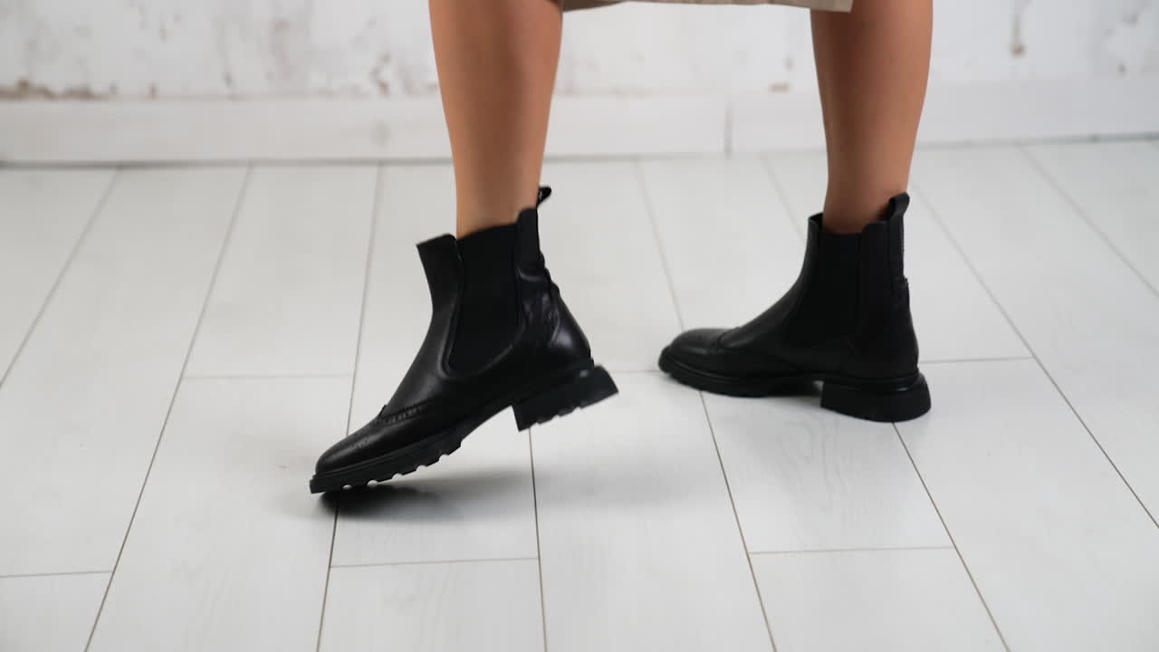 Lady in beige coat and black leather boots. Woman walks in the studio demonstrating comfortable stylish autumn look and footwear. White backdrop.