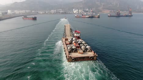 barge loaded with concrete mixer trucks pulled to port by a tugboat in hong kong bay, aerial view