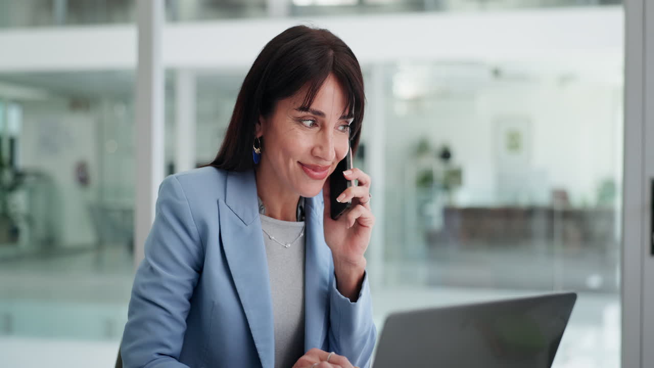 Professional Woman Talking on Phone While Working on Laptop in Office
