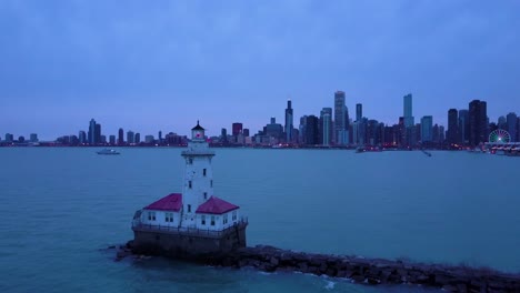 Una-Hermosa-Antena-Nocturna-Alrededor-De-Un-Faro-Icónico-En-El-Lago-Michigan-Con-La-Ciudad-De-Chicago-Distante