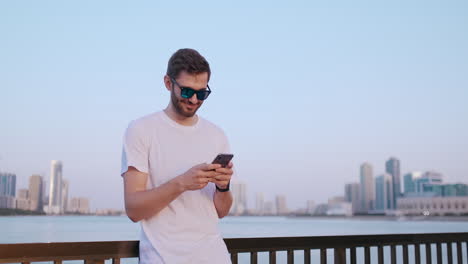 Attractive-and-handsome-young-man-with-beautiful-smile-and-hipster-millennial-generation-z-looks-scrolls-through-social-media-feed-on-smartphone-giggles-and-smiles-from-news-on-applications.