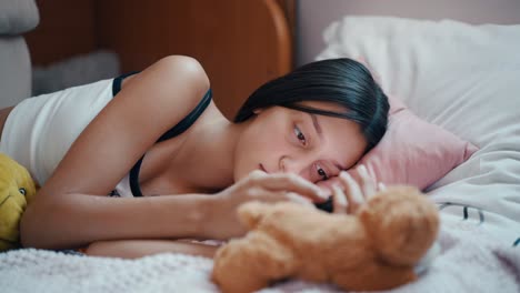 a teenage girl lies lazily on her bed, scrolling through social media on her phone