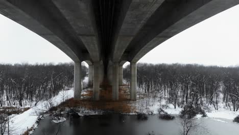 a drone flight between columns of pace bridge in missouri, over a snowy lake