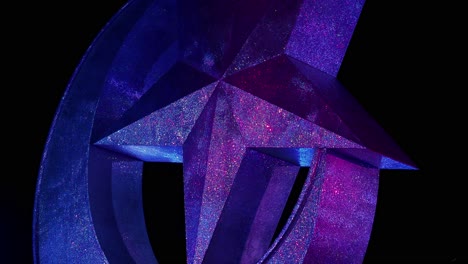 low angle of glittery star and crescent statue lit by colorful lights at night