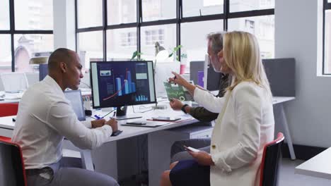 Diverse-business-people-sitting-using-computer-and-takling-at-desk-in-office