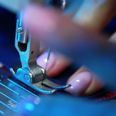 female hand pushes material through a sewing machine. sewing machine needle rapidly moves up and down. tailor sews blue fabric in the sewing workshop. close-up