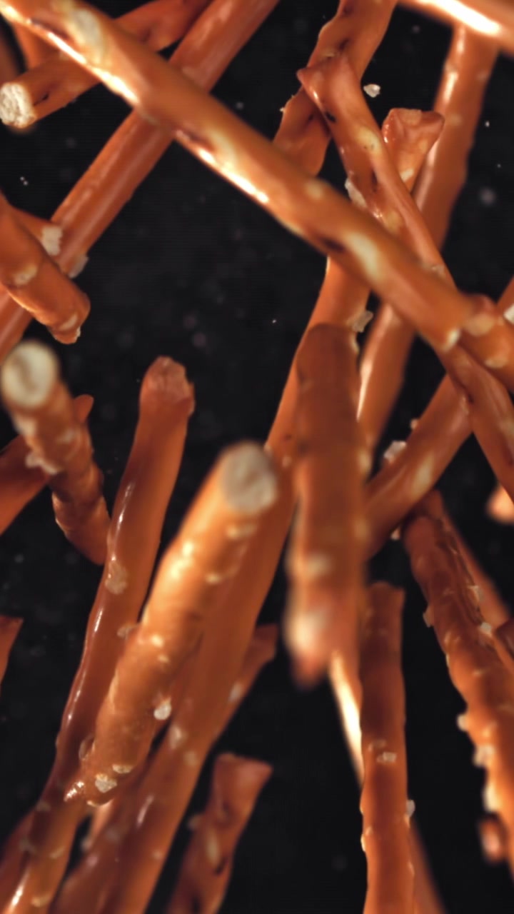 Palitos de pretzel salgados caindo em câmera lenta sobre fundo preto