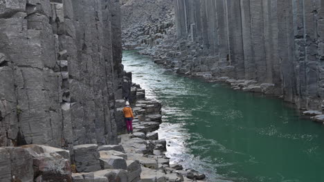 Eine-Person,-Die-Auf-Basaltfelsen-In-Einer-Schlucht-Mit-Grünem-Fluss-Und-Basaltsäulen-Herumläuft-Und-Sich-Umschaut