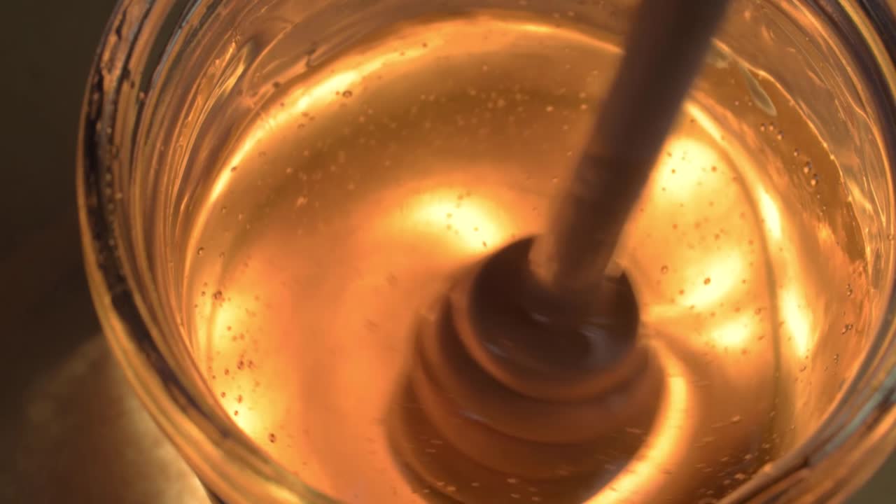 Primo piano di un cucchiaio che versa miele dorato e liquido in un barattolo di vetro