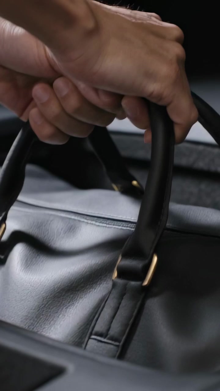 Video vertical: Manos extendiéndose ajustando el agarre en las asas de un bolso de lona de cuero en el coche, preparándose para salir