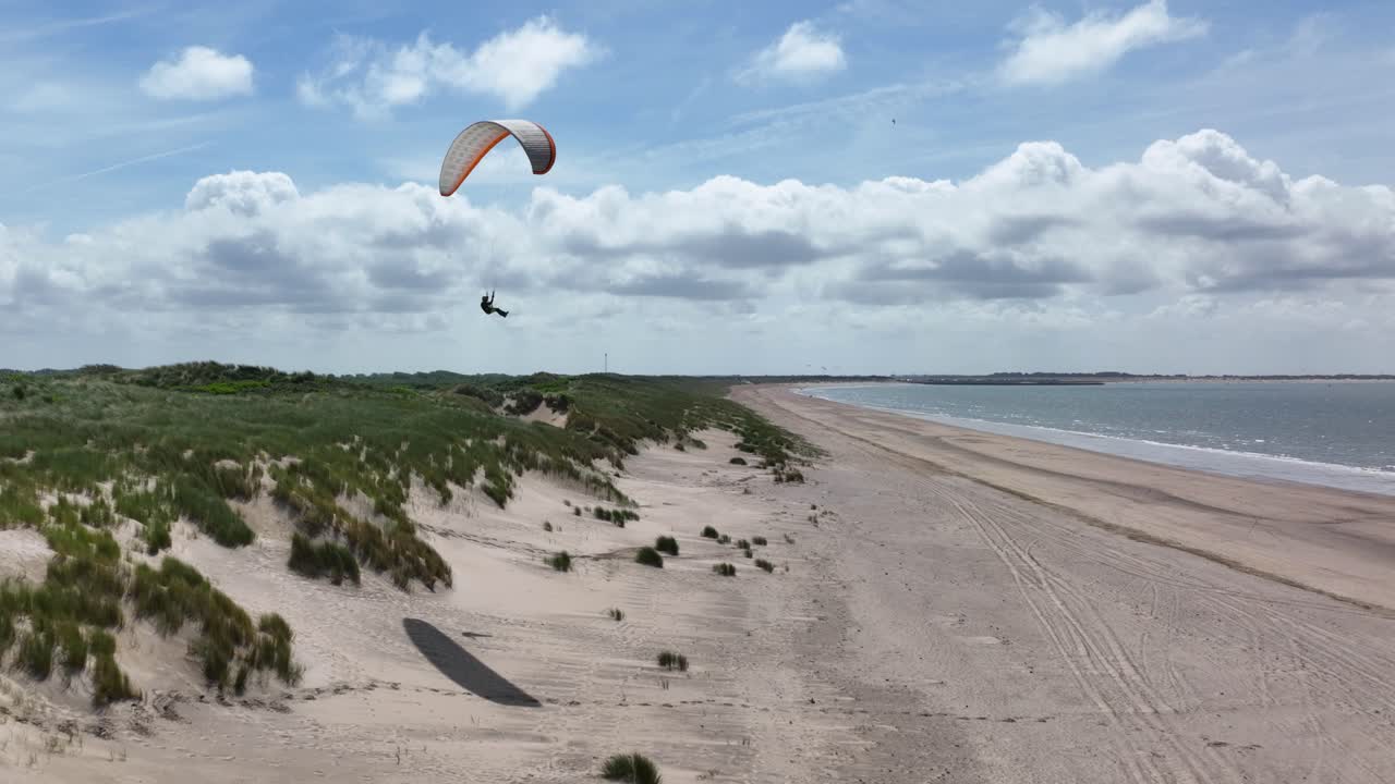 дрон отслеживает полет параплана вдоль голландских песчаных дюн на набережной в лучах солнца