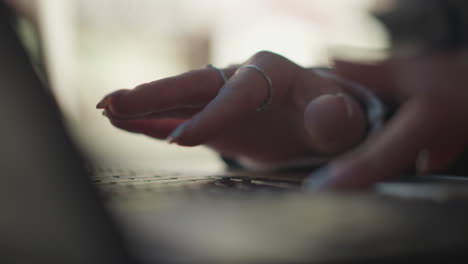 close-up of hands with polished nails, delicate rings, and elegant fingers typing on laptop keyboard outdoors, with soft background blur