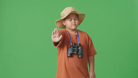 모자와 안경을 입은 아시아 관광 소년은 머리를 흔들고 손을 흔들며 어떤 몸짓도 보여주지 않고 녹색 화면 배경에서 제안 피합니다. 소년 연구자, 여행 관광 모험 개념