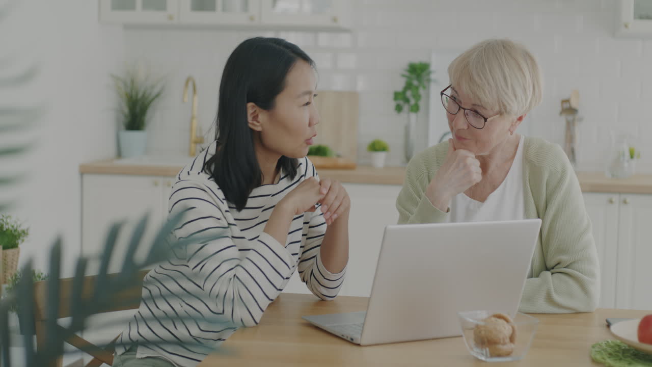 Two women in kitchen using laptop