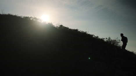 man walking uphill with a backpack, silhouette feeling with bright sun behind