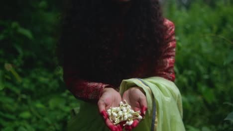 close-up of a woman holding white flowers in her hands, with henna-stained fingers. the camera tilts down toward her hands. she wears a green dupatta and red patterned sleeves