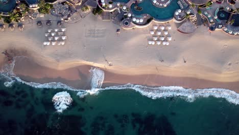 a resort beach in a tropical paradise with swimming pools and cabanas - straight down ascending aerial view