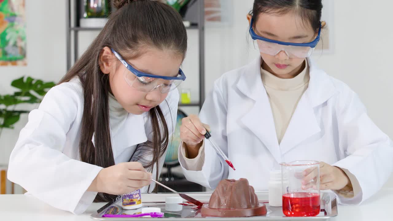 Siswa sekolah dasar mengenakan kacamata pengaman menggunakan pipet untuk melakukan eksperimen gunung berapi di ruang kelas.