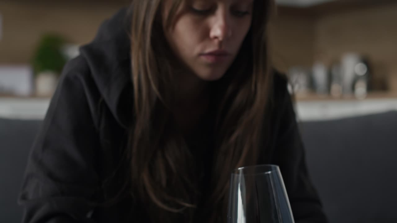 una mujer caucásica triste con problemas con el alcohol sosteniendo un vaso de vino tinto.