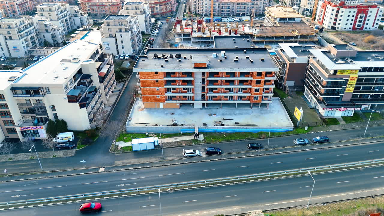 Vista aérea de um canteiro de obras de um edifício residencial à beira da estrada. Um longo prédio de apartamentos de tijolos vermelhos em construção, situado ao lado de uma estrada asfaltada de várias pistas em uma cidade costeira.