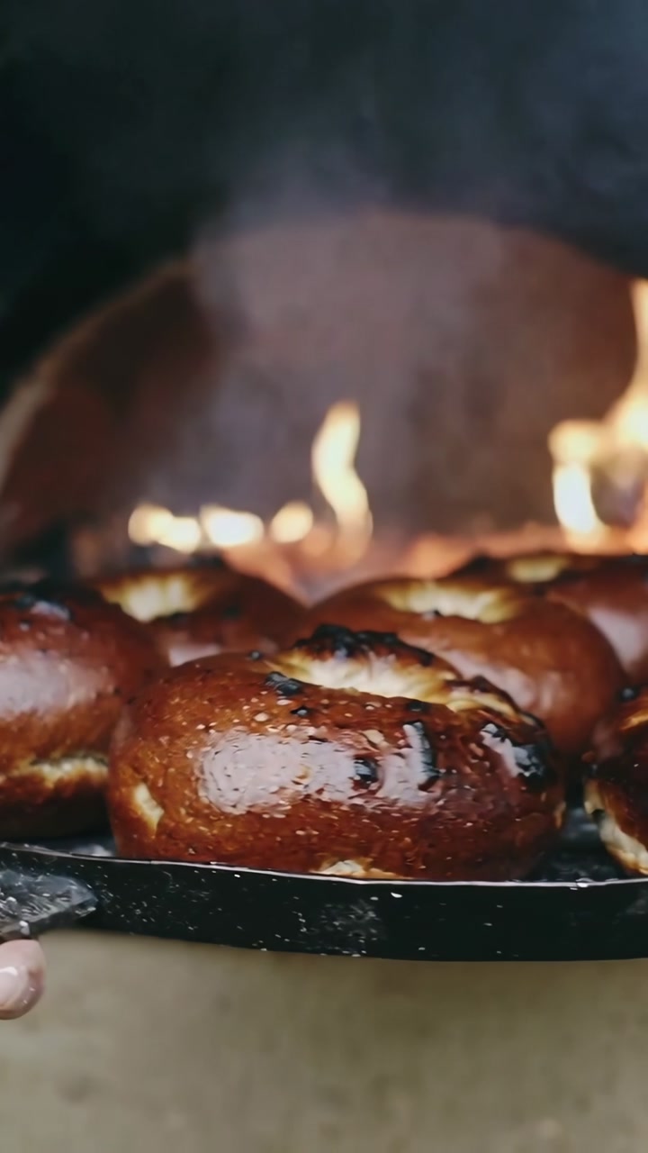 Vertical video: Pulling baker hands checking doneness of rolls from wood-fired oven on metal tray