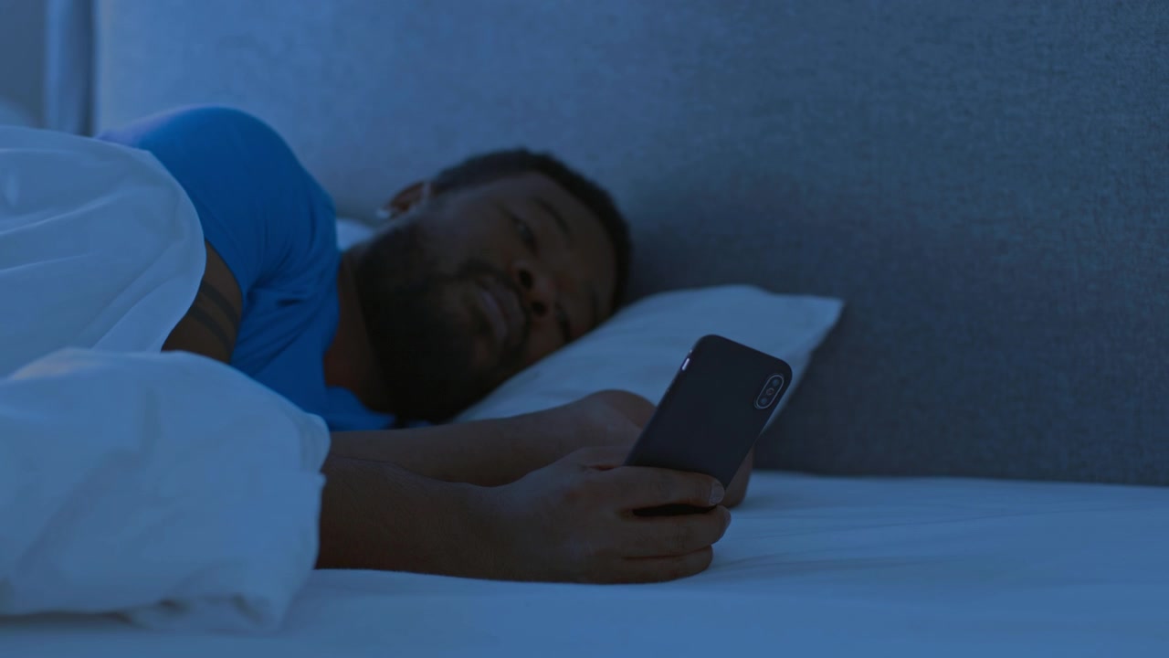 Giovane uomo che usa lo smartphone mentre è sdraiato a letto di notte