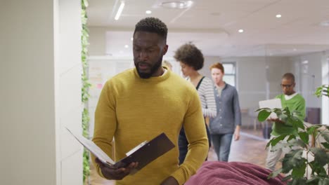 african american creative businessman holding documents and walking in modern office