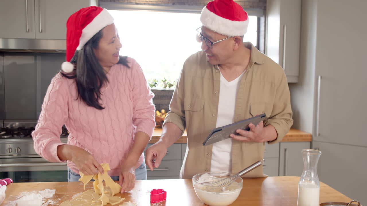 Baking Christmas cookies, senior asian couple wearing Santa hats, smiling joyfully together