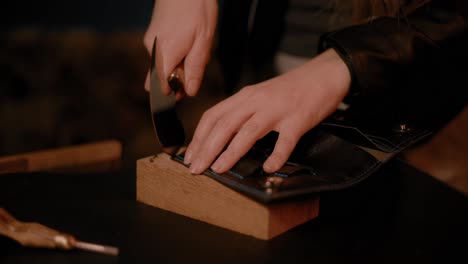 Woman-hands-using-a-round-head-knife,-cutting-leather-in-the-workshop,-dark-setup,-high-contrast,-color-graded