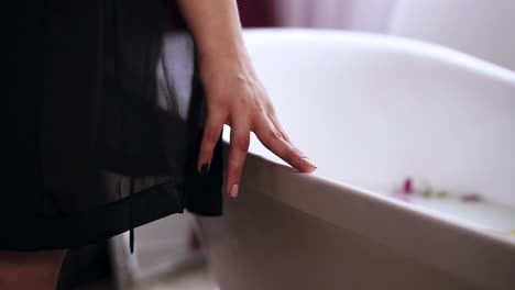 젊은 매력적인 여성이 욕조에 올라와 우유와 꽃으로 가득 찬 따뜻한 목욕을 준비하고 있습니다. 느린 움직임