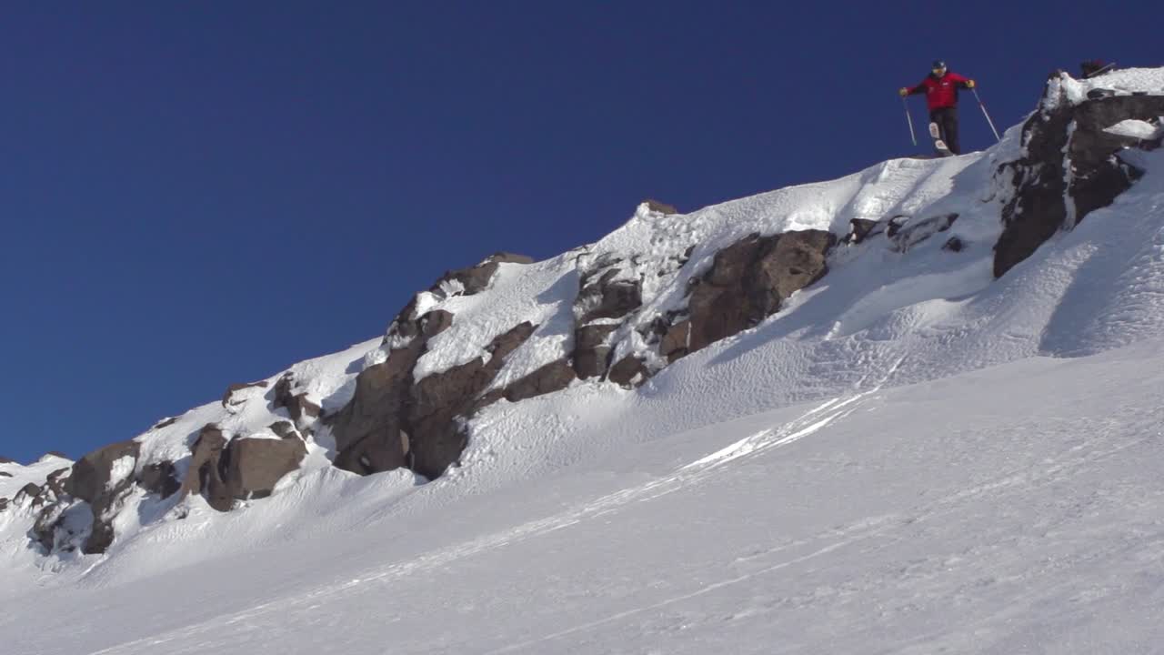 esquiador freeriding extremo saltando desde un acantilado realizando un truco de agarre en el aire, lento