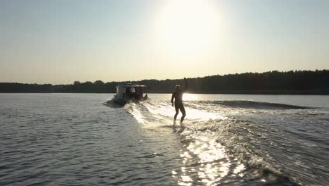 Surfer-on-surfboard-surfing-waves-behind-boat-in-sunset-002