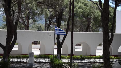 flag of greece flying at avenue with traditional white building in background and car passing by