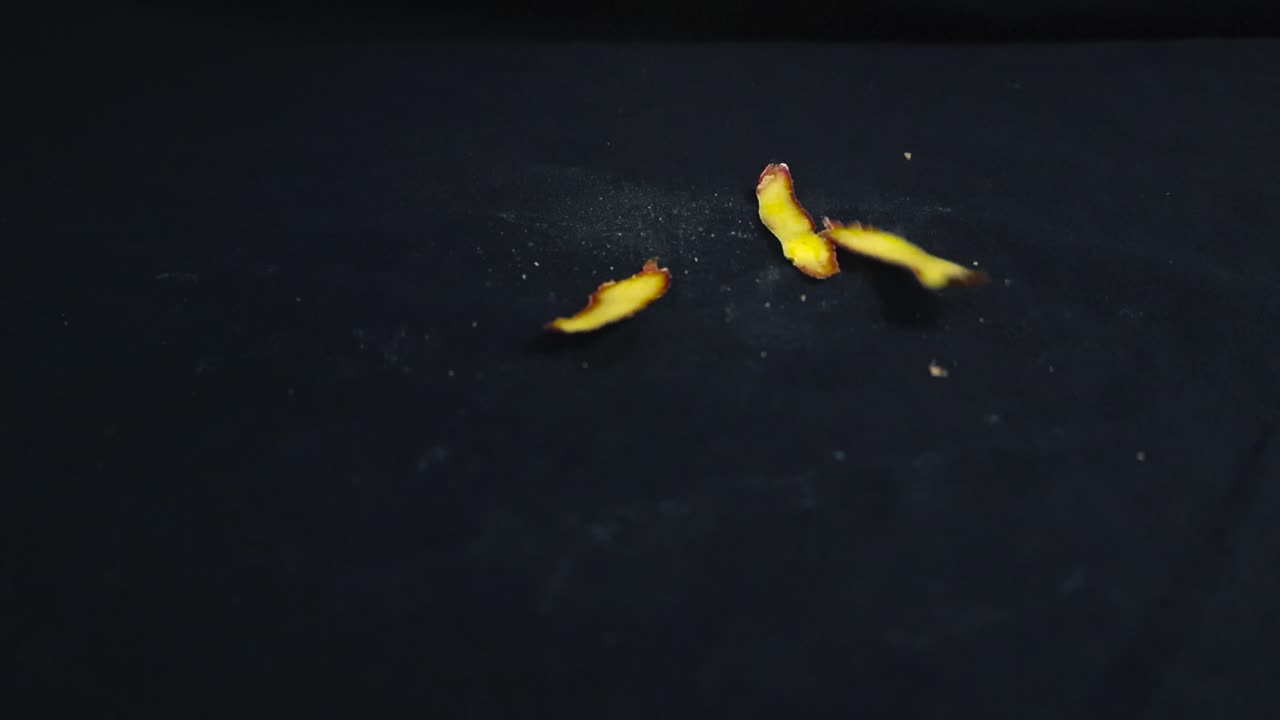 Slow motion video of dirt covered and yellow colored potato peels falling on a black background after potato peeling. dust flying