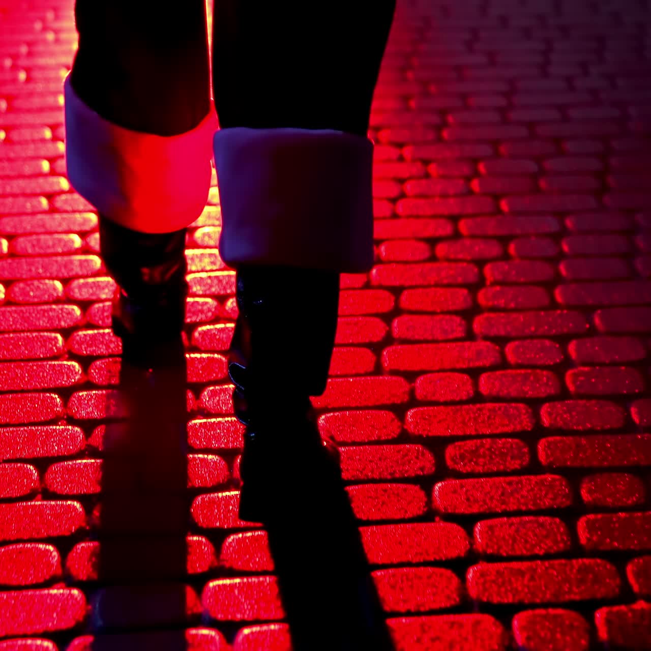 Santa Claus walk on pavement. Legs of Father Frost at Christmas outdoors. Boots of Santa walking on a pavement at dark. Red lighting. Back view