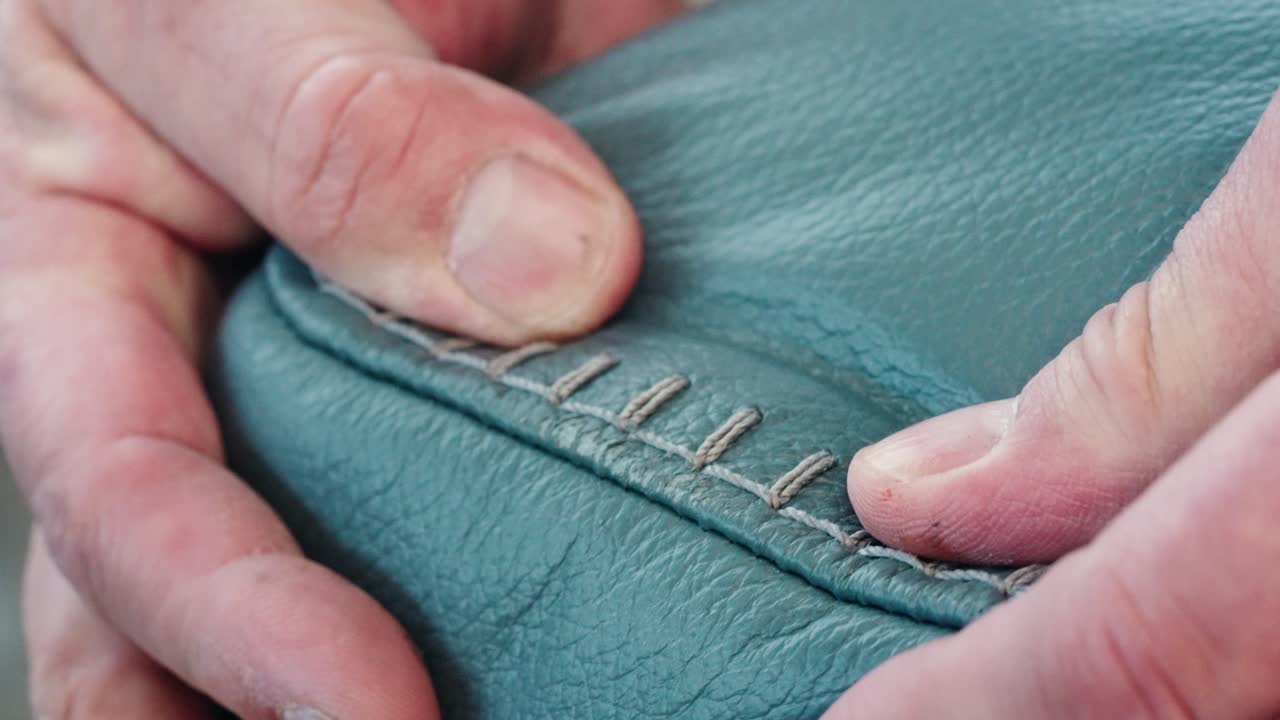 Hand squeezes blue leather arm, revealing scratch near white stitching