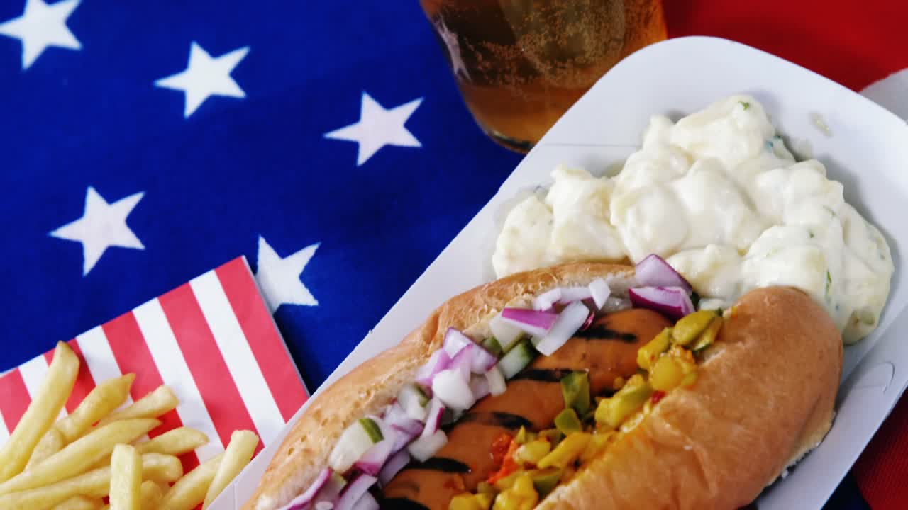 perrito caliente, papas fritas y un vaso de cerveza servidos con bandera estadounidense