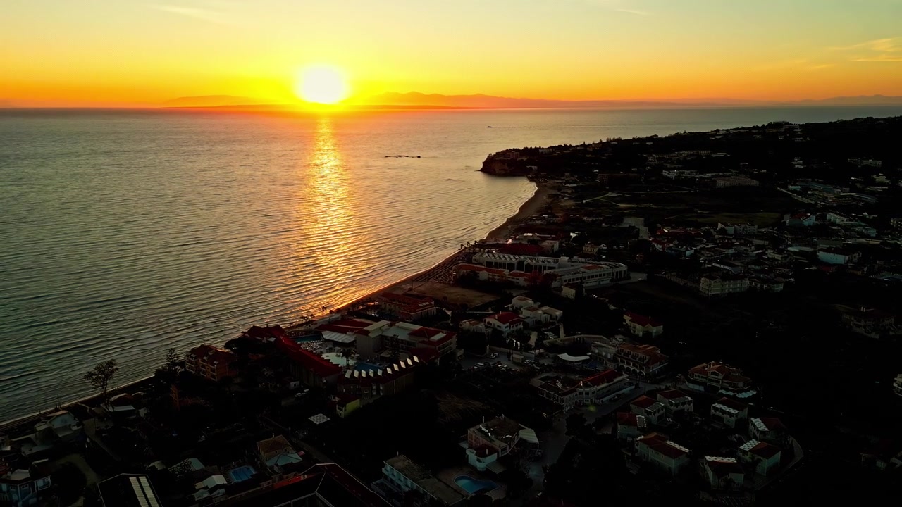 Vista del tramonto sull'oceano e una costa scura con acqua calma e cielo sereno.