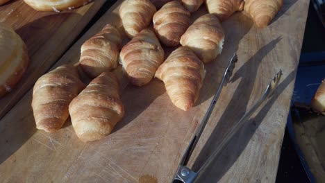 golden brown croissants, displayed on wooden cutting boards, are progressively arranged, creating a visually appealing presentation alongside tongs for serving